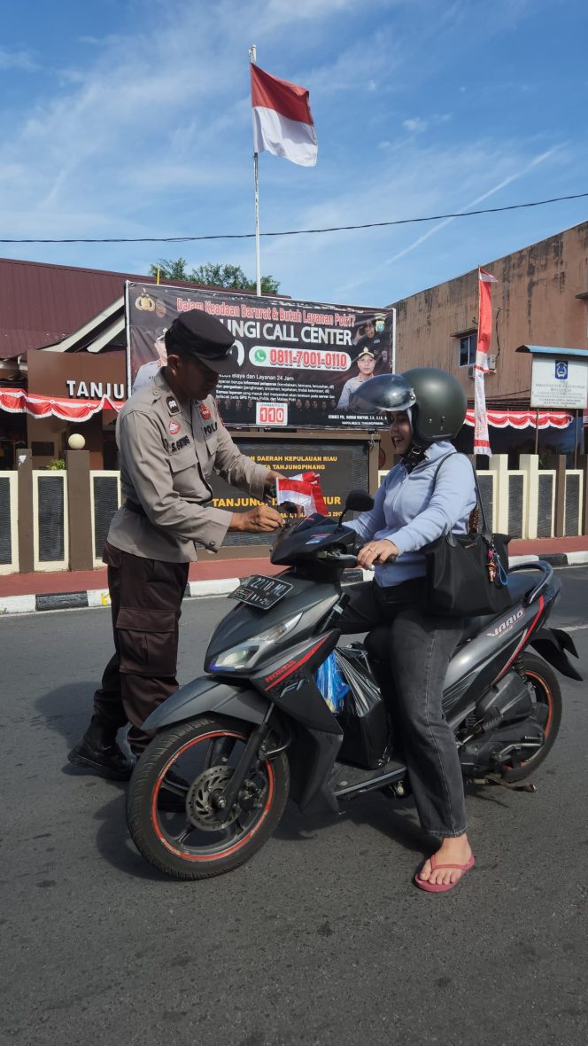 
					Anggota Polsek Tanjungpinang Timur saat membagikan bendera merah putih kepada pengendaraan bermotor, Sabtu (02/8/2025). (Humas Polres Tanjungpinang)